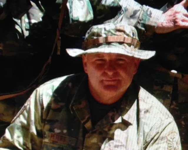 A man in fatigues and a hat is smiling.